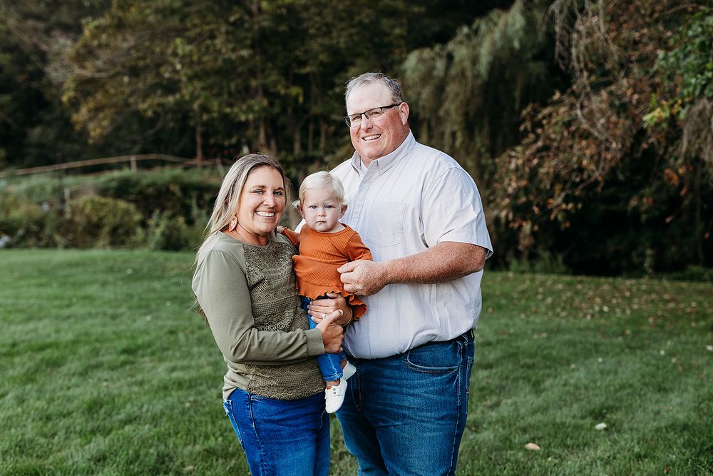 Casual autumn family portrait taken outdoors on green grass with trees in background.