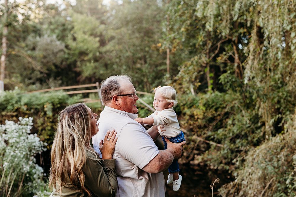 People enjoying a tender family moment outdoors near a willow tree in a garden setting during golden hour.