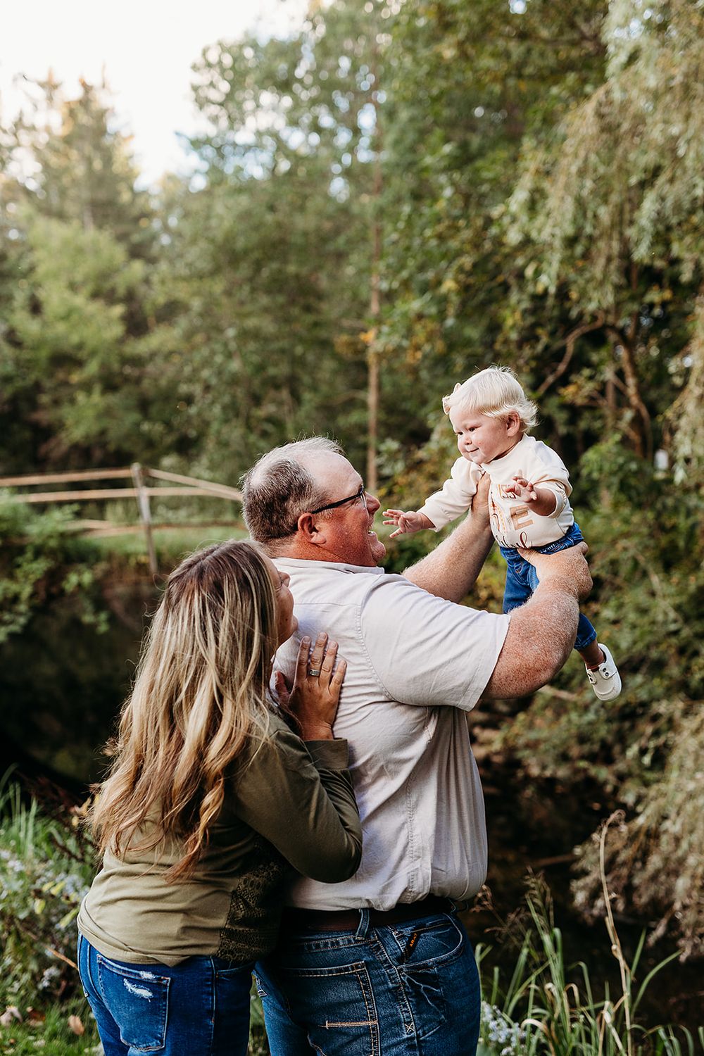 A couple shares a sweet outdoor moment with their baby in a natural wooded setting during golden hour.