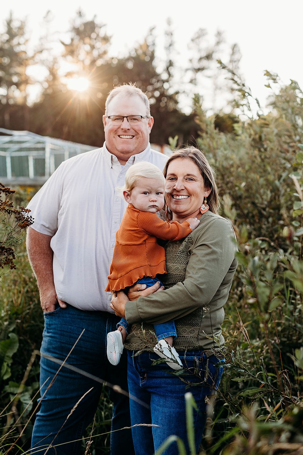 A multigenerational family poses together in an outdoor garden setting at sunset with sunlight shining through trees.