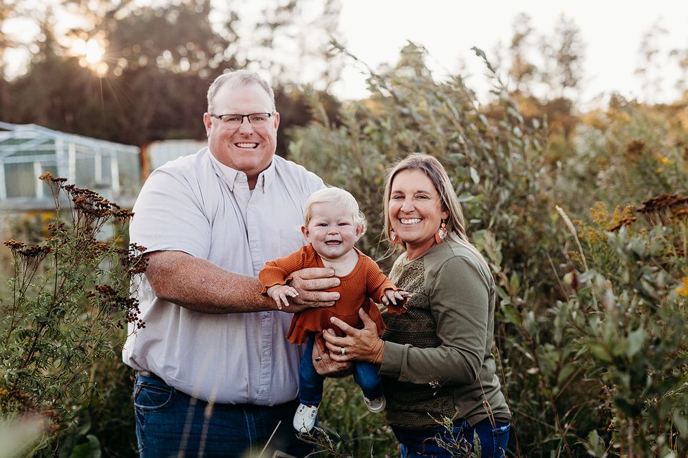Fall family photo session outdoors in a rustic garden setting with pumpkins at sunset.