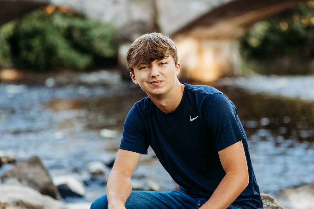 A person in a navy Nike t-shirt sits by a flowing river on a sunny afternoon.