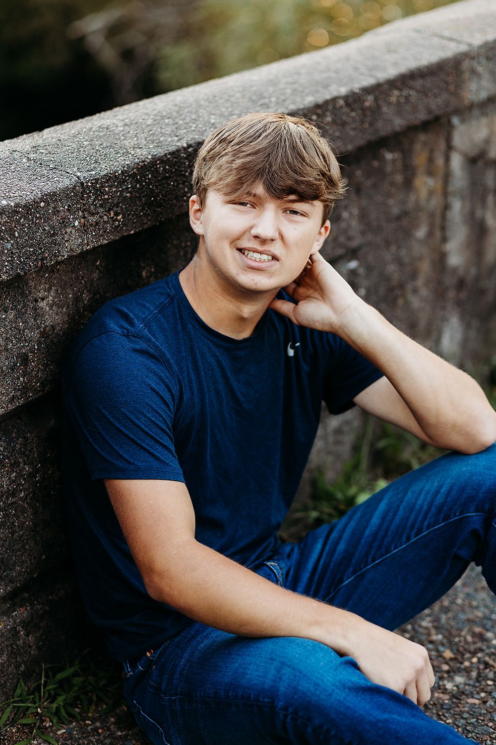 A person sits comfortably on concrete steps wearing a navy t-shirt and jeans during an outdoor photo session.
