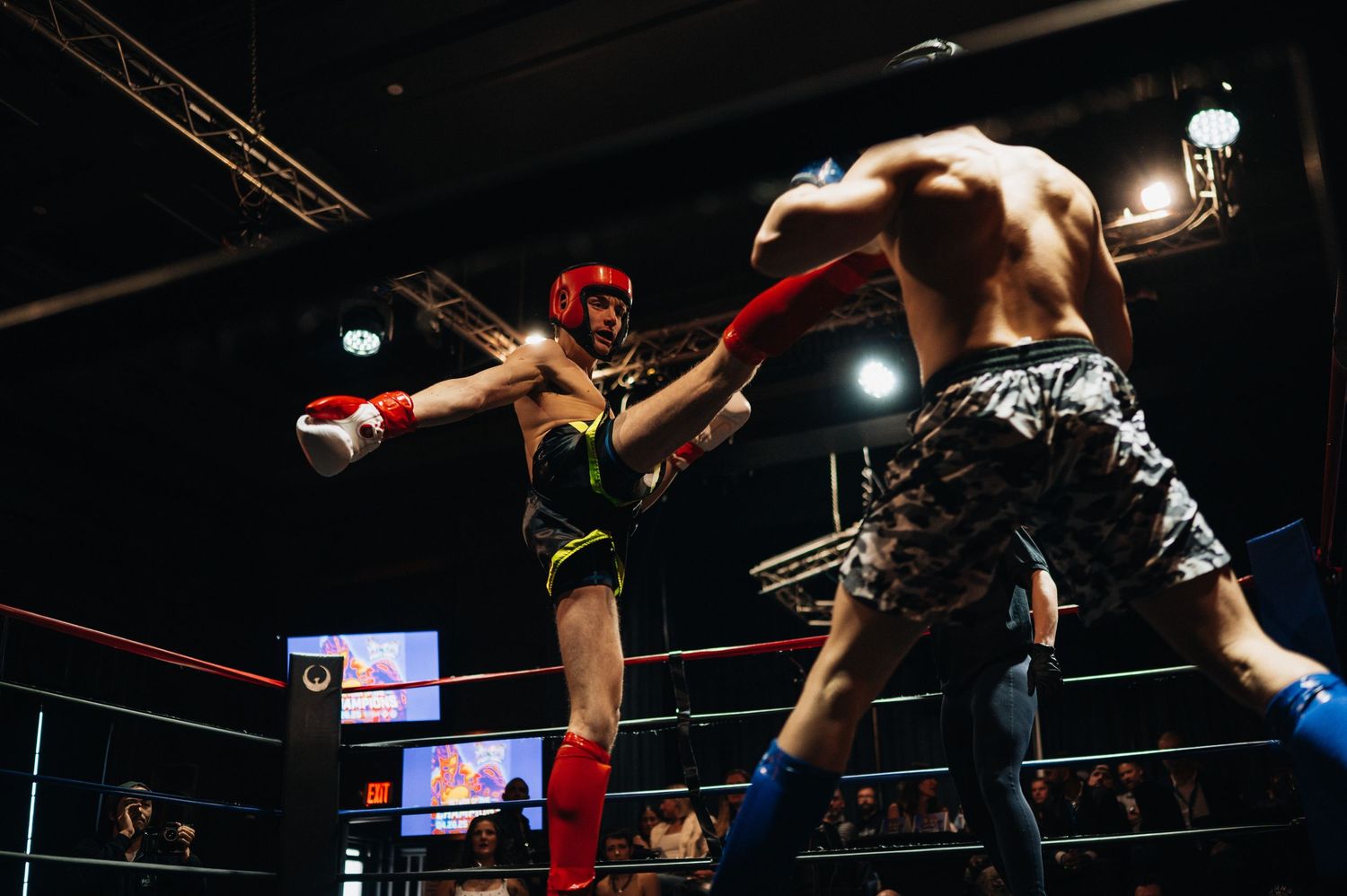 Two masked wrestlers face off in an intense wrestling match with dramatic lighting in a dark arena.