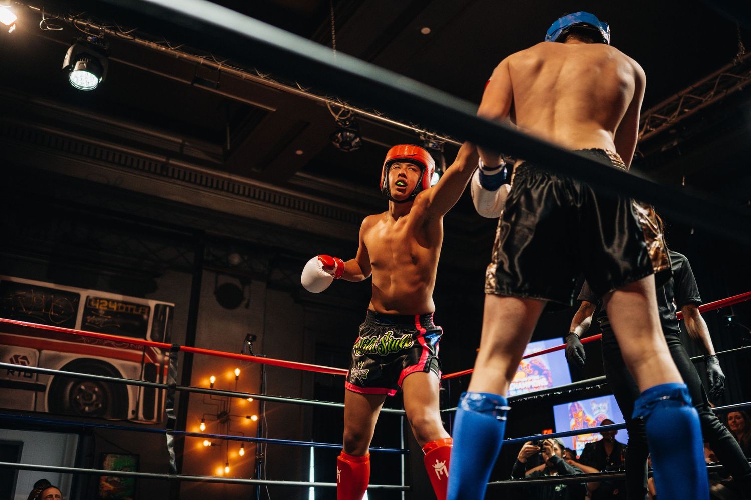 Two martial artists square off in a boxing ring during a competitive fighting match with dramatic lighting.