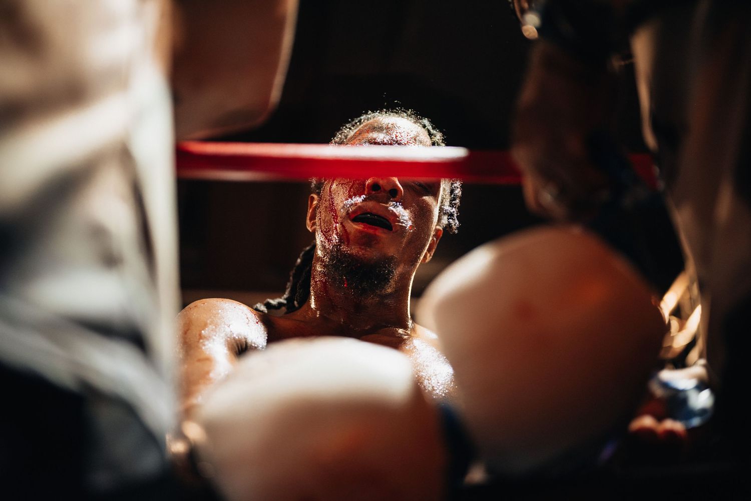 A boxer receiving medical attention between rounds with a red straw and dark shadows in the background.