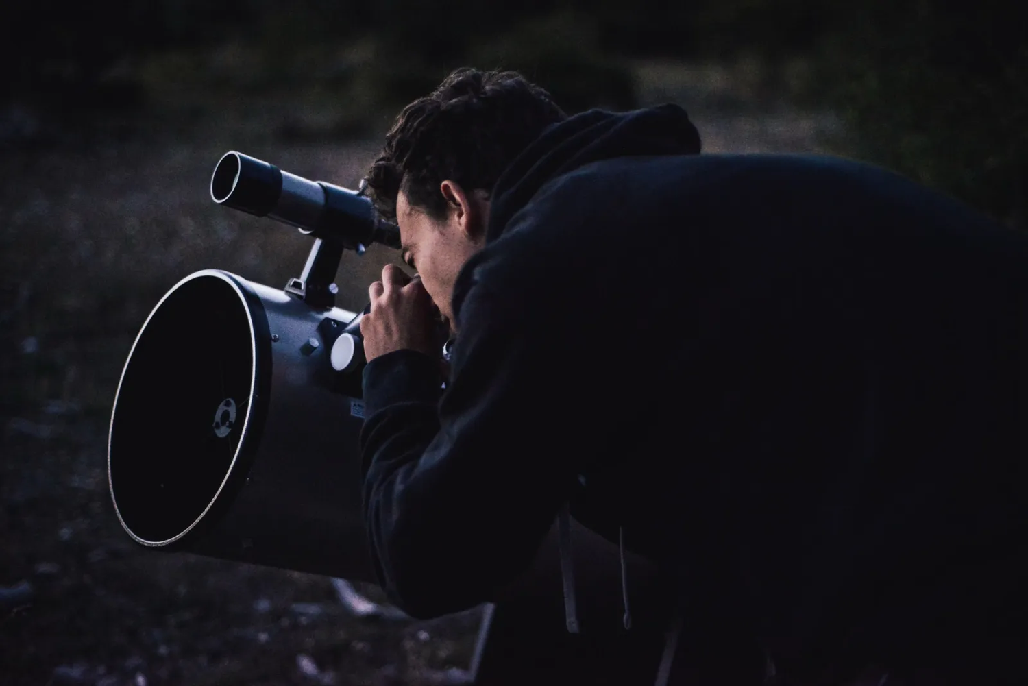 Personne penchée sur un grand télescope en pleine nuit, concentrée sur l’observation du ciel.