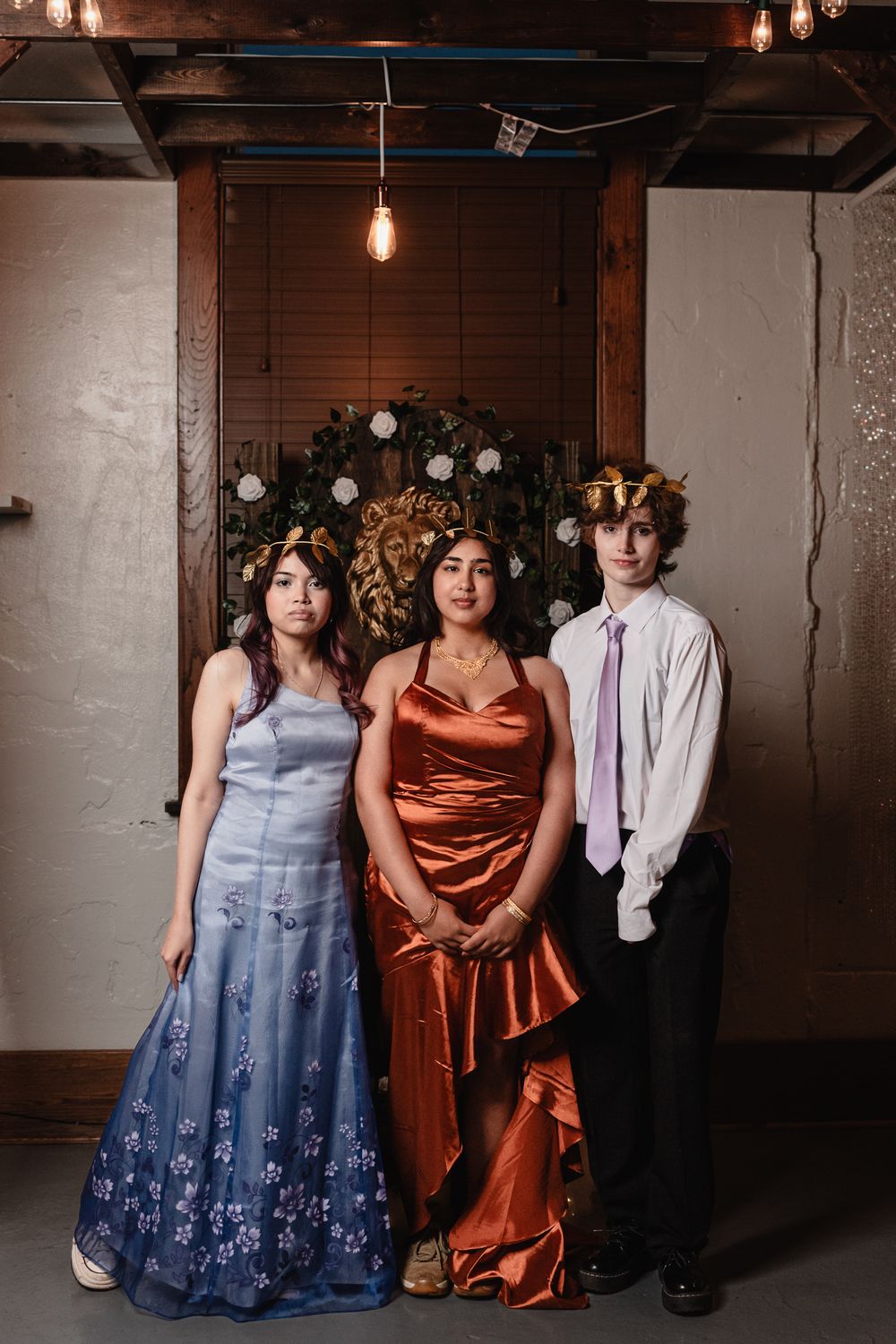 Three nicely dressed people pose together in front of a decorated wall at a formal event in elegant dresses and suits.