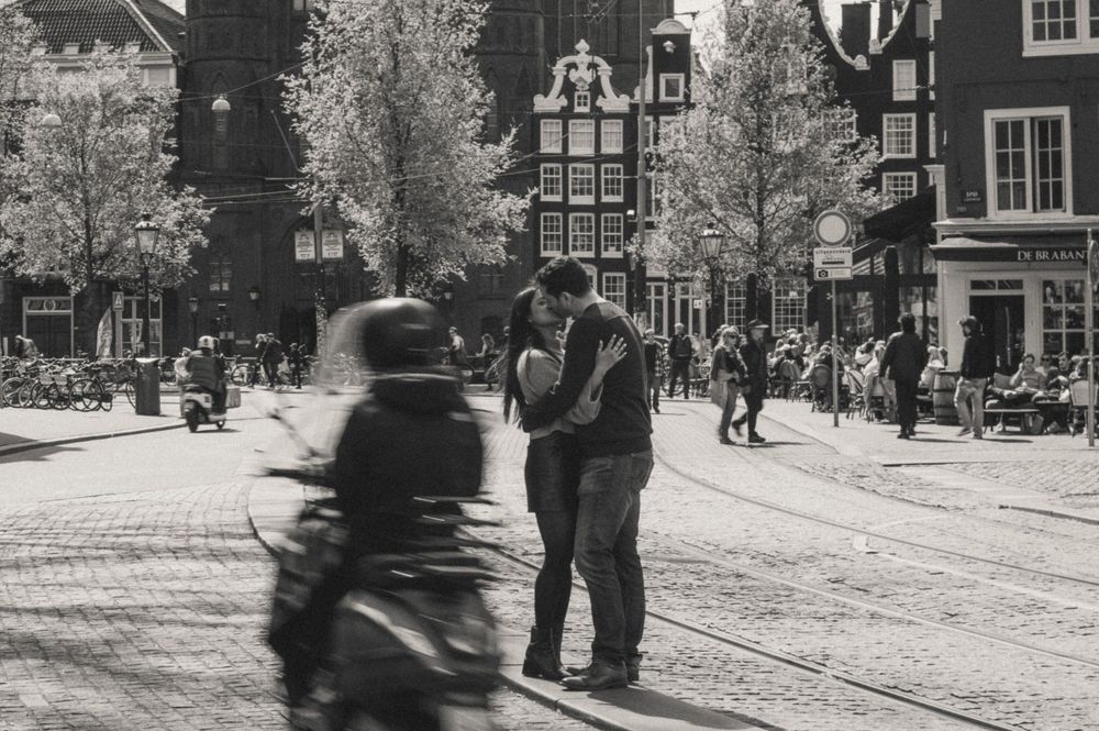 A black and white street scene in Amsterdam with people and historic buildings.