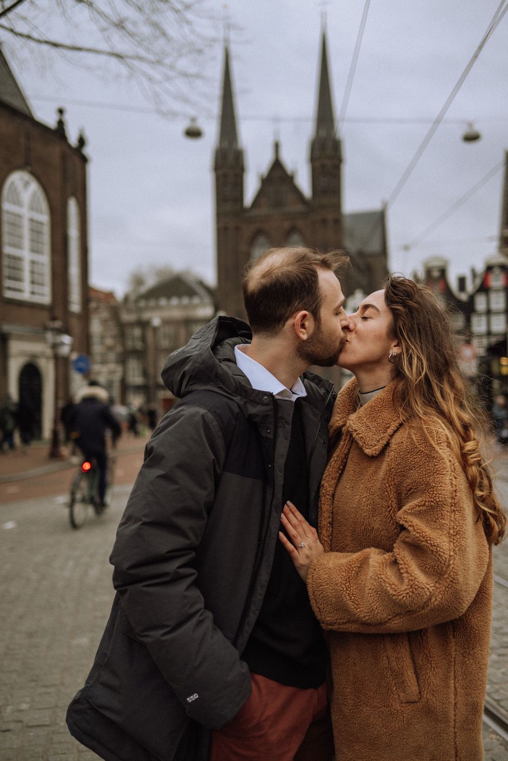 Couple sharing intimate moments on a cobblestone street with church spires in the background.