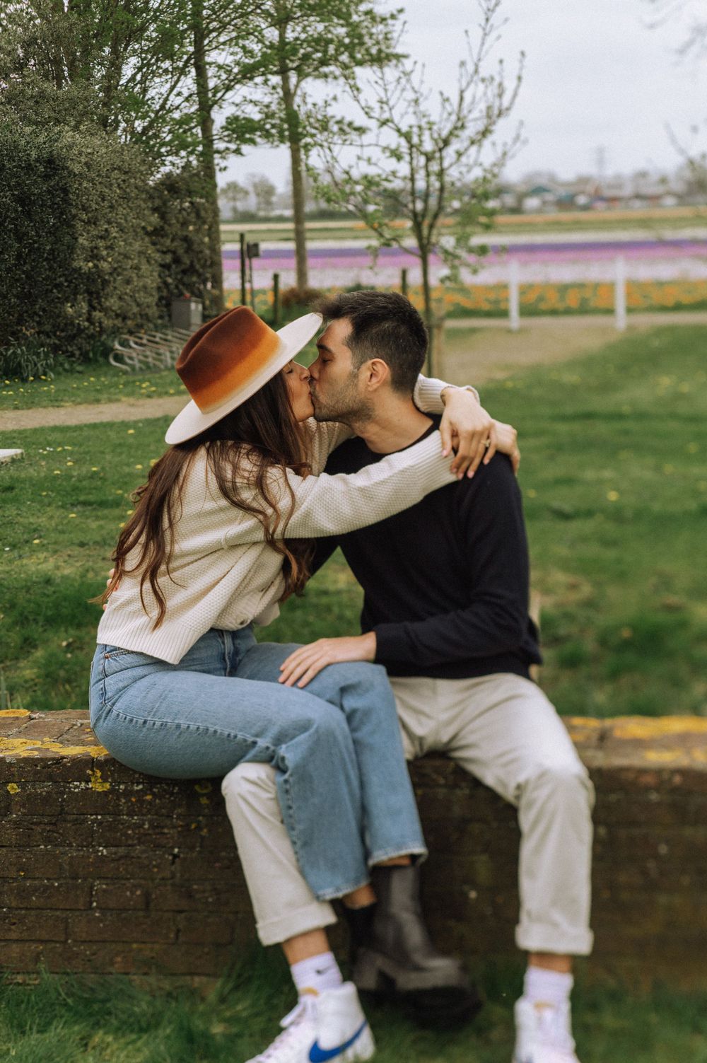 Couple sharing intimate moments while sitting on brick wall in park setting.