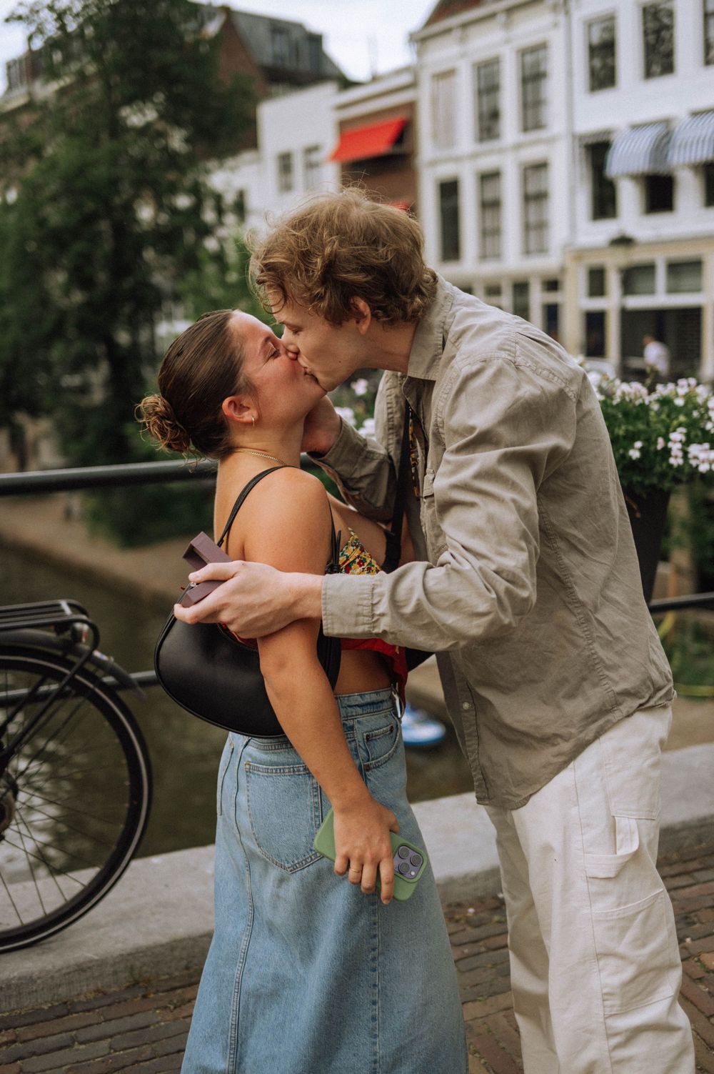 A romantic embrace by a canal with bicycles and historic buildings in the background.