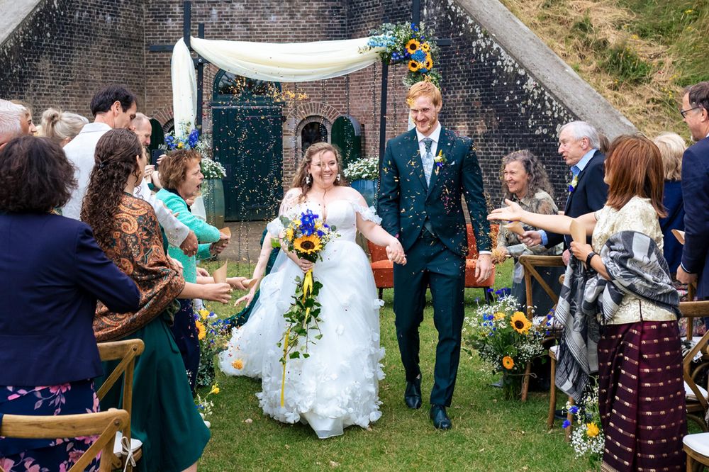 Trouwreportage met confetti na de ceremonie terwijl het bruidspaar richting de bruidstaart loopt