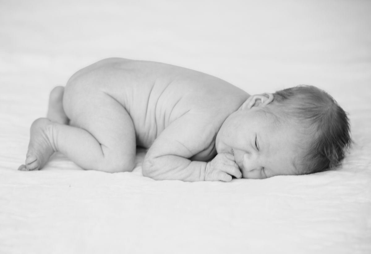 Black and white photo of sleeping newborn baby lying on white blanket.
