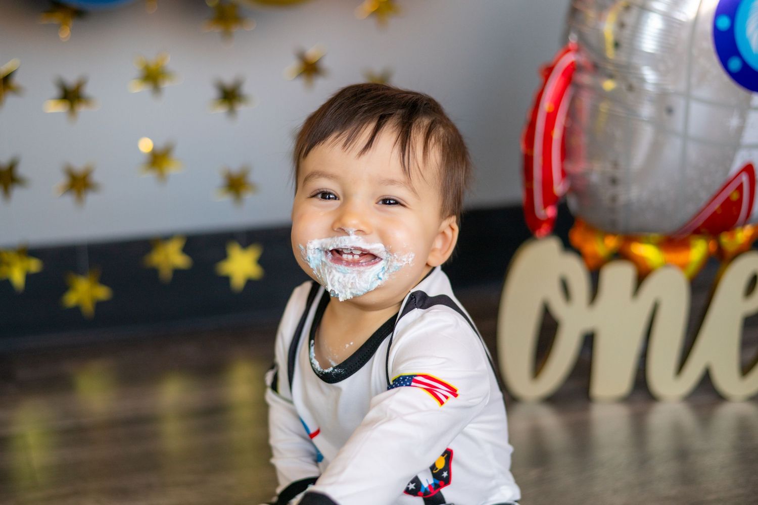 A small child in white clothing smiles with whipped cream or frosting on their face against a starry background.