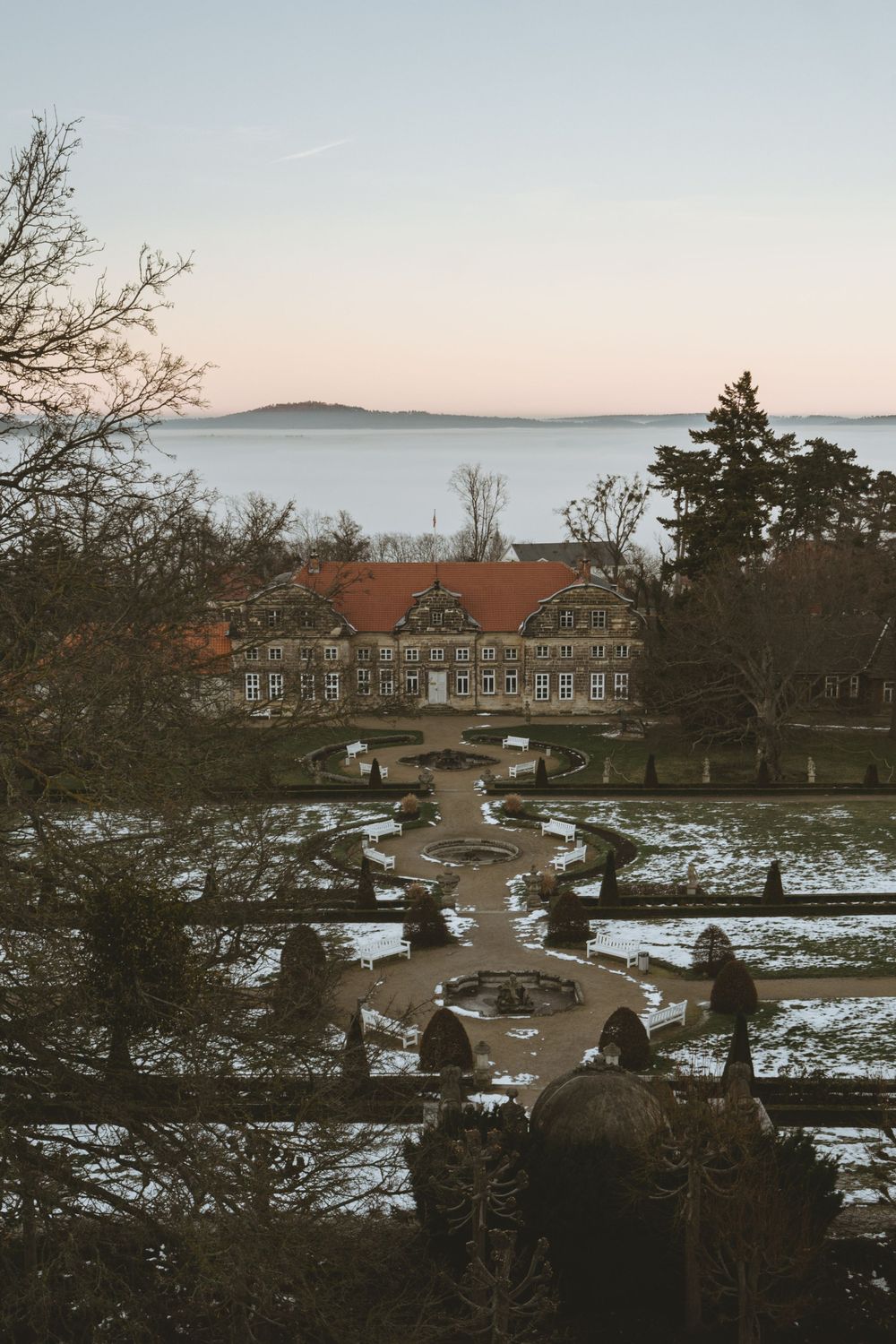 Aerial view of grand historic building with snow-covered garden paths leading to waterfront.