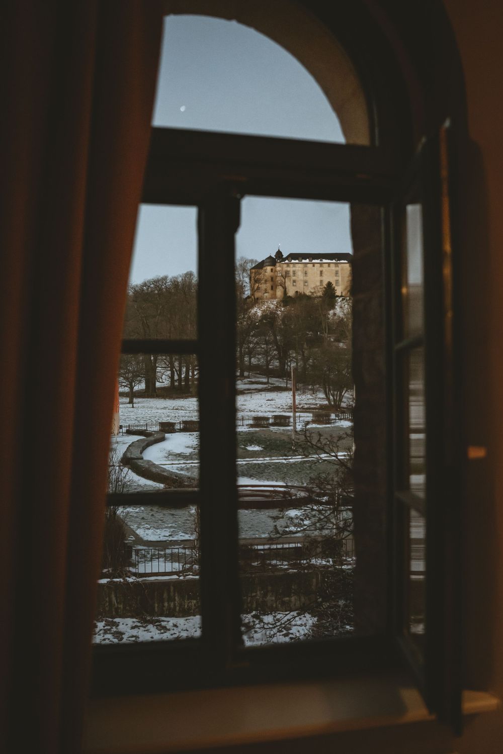View of a grand castle through an arched window on a snowy winter day.