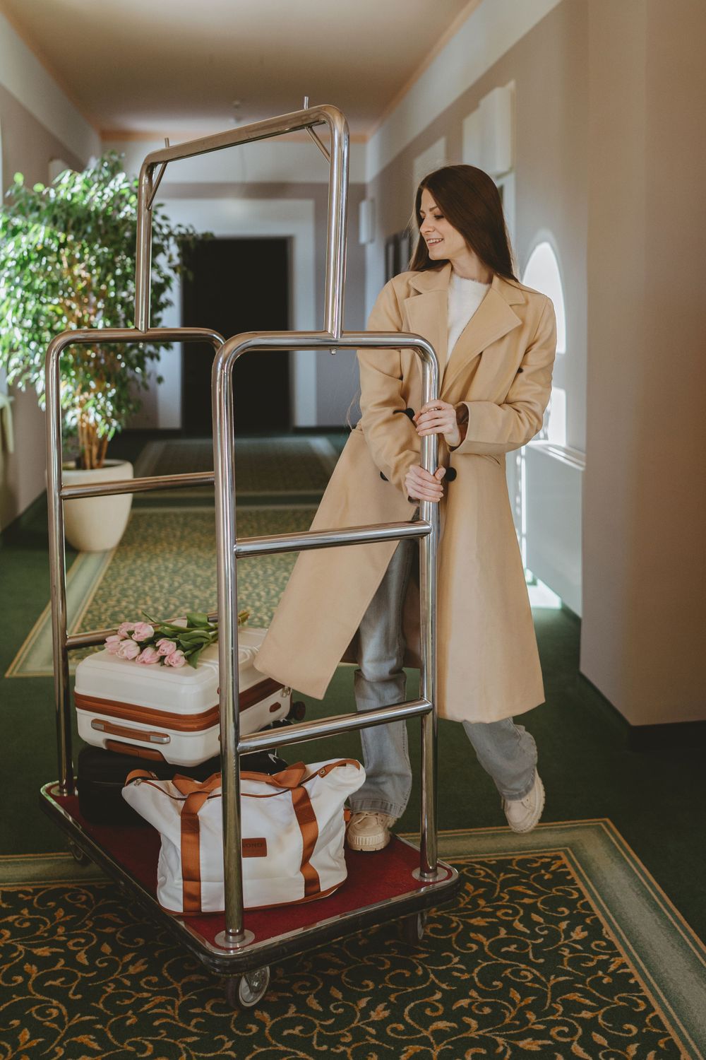Elegant hotel luggage cart with cream colored coat and travel bags in luxurious hallway.