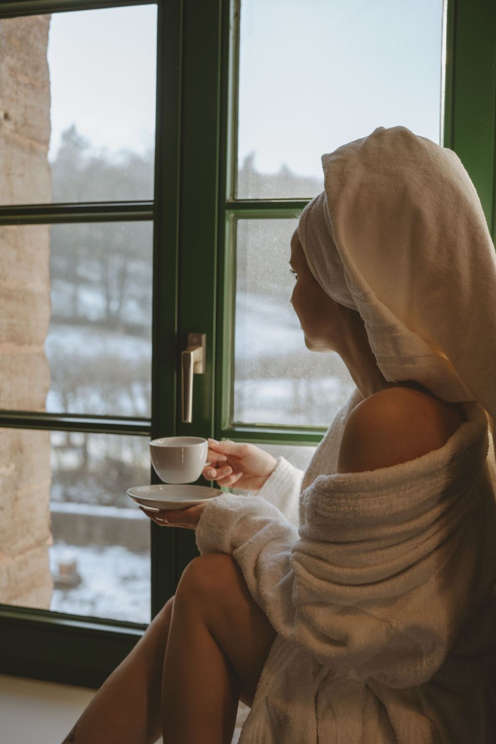 Relaxing winter morning scene with robe-clad figure enjoying coffee by frost-covered window.