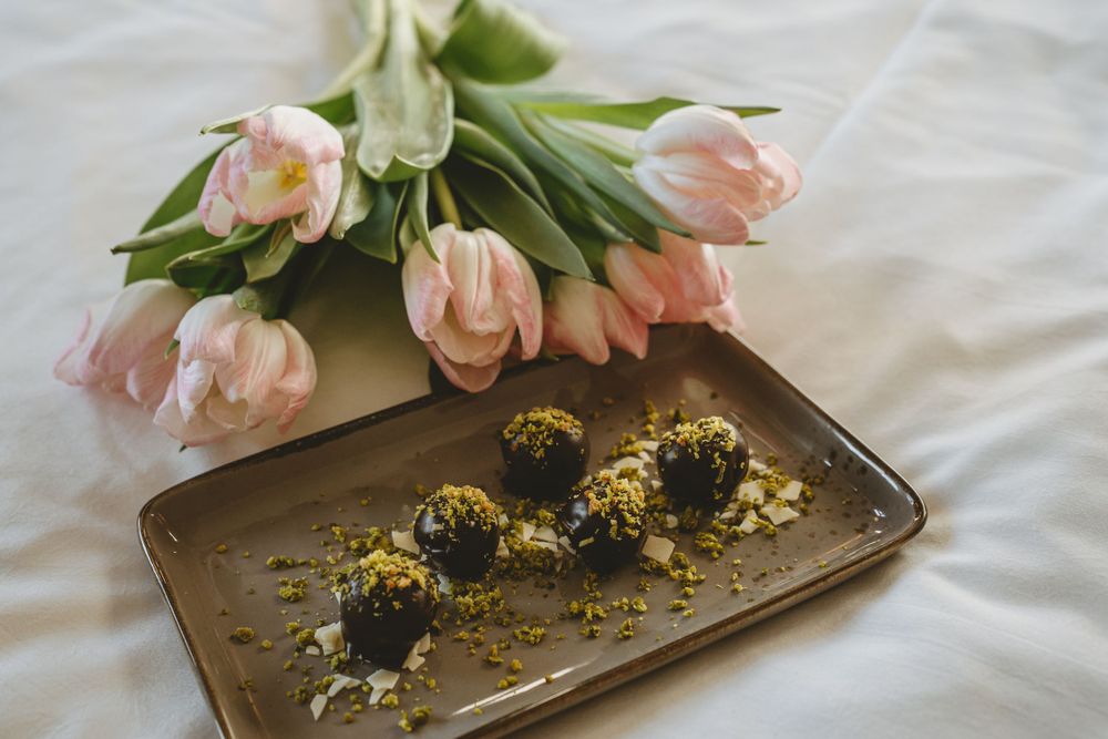Pink tulips and chocolate truffles arranged on bronze serving tray against white background.