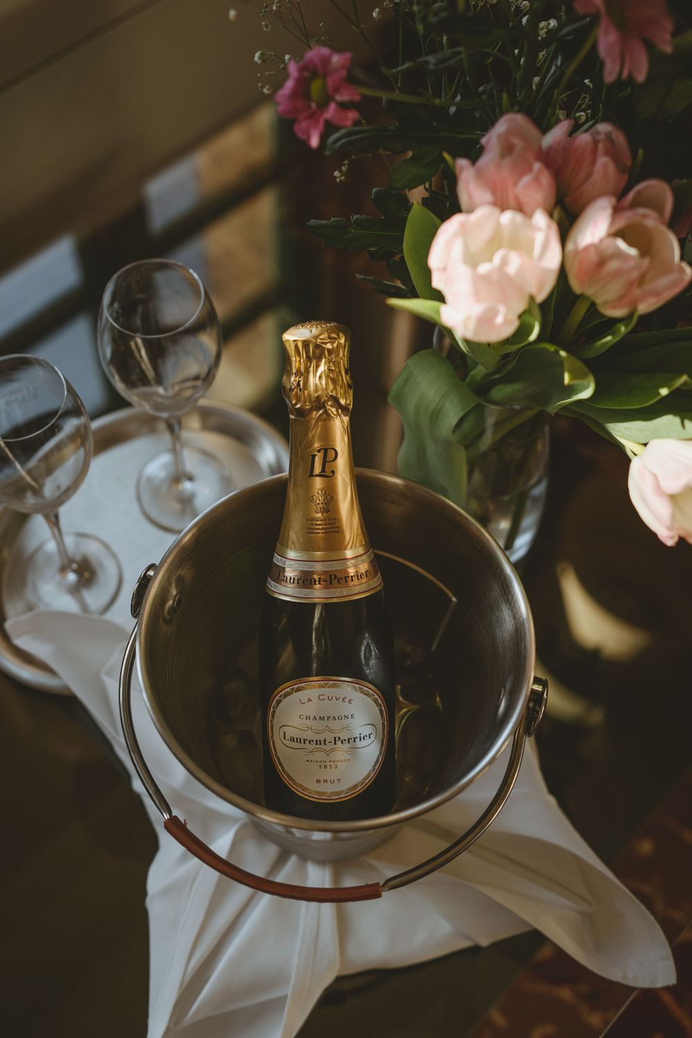 Champagne bottle chilling in an ice bucket with pink roses and wine glasses.