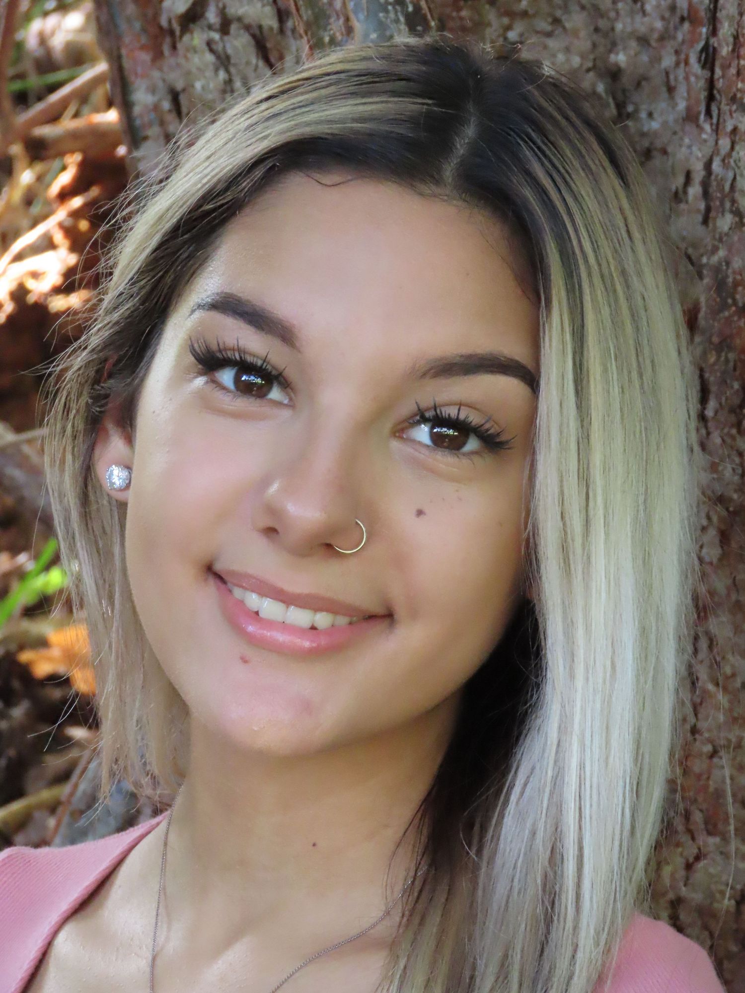 A portrait against a tree trunk showing platinum blonde hair and natural makeup.