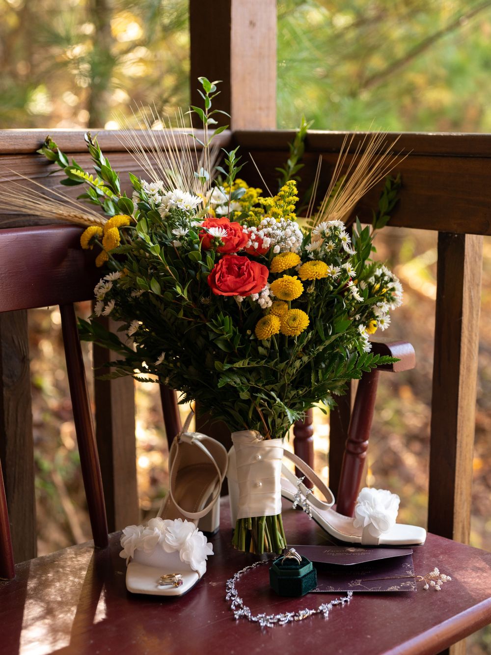 Wedding details with bridal bouquet, shoes and jewelry arranged on wooden deck chair.