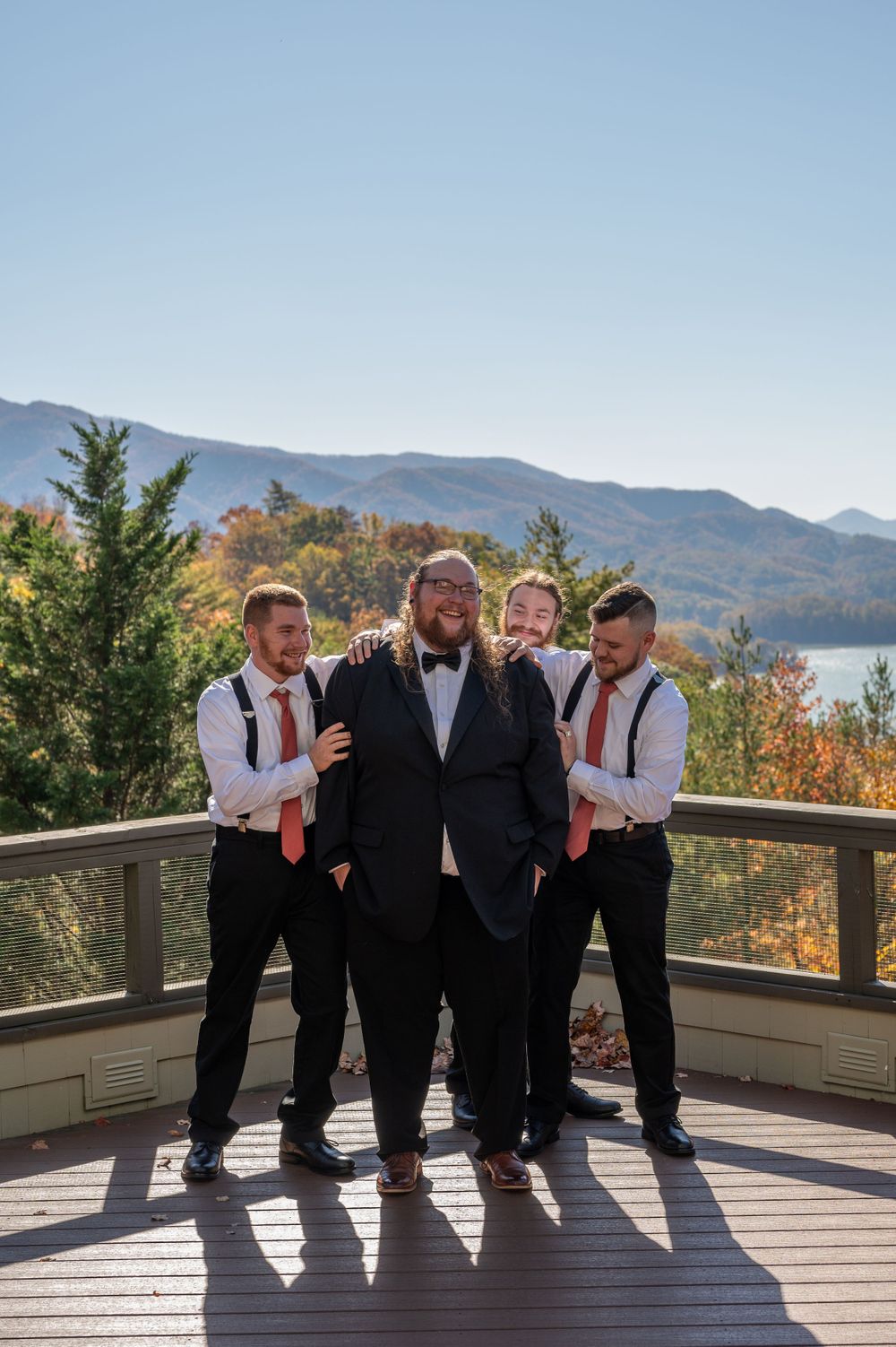 Wedding party of groomsmen posing together on mountain deck with scenic autumn backdrop.