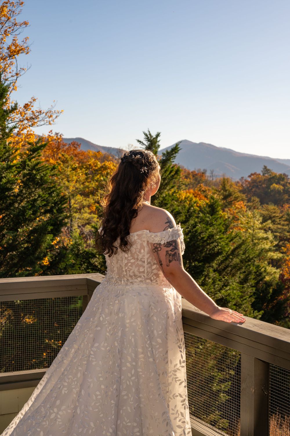 Back view of bride in lace gown overlooking mountain landscape with fall colors.