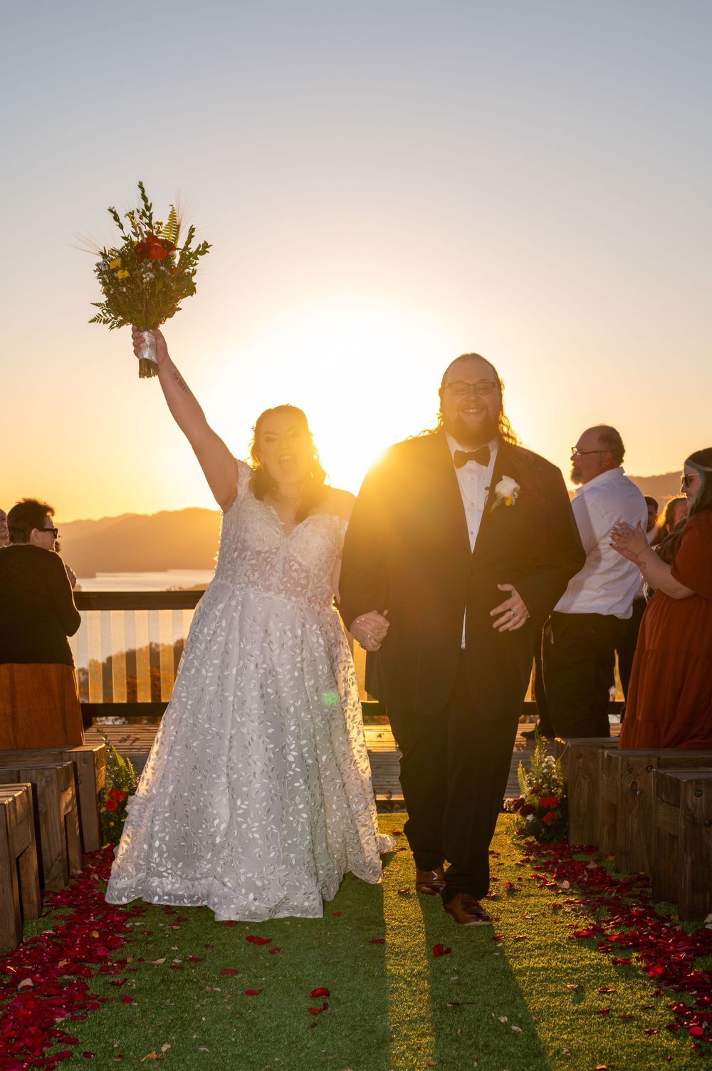 Triumphant wedding recessional at sunset with mountain backdrop and rose petals.
