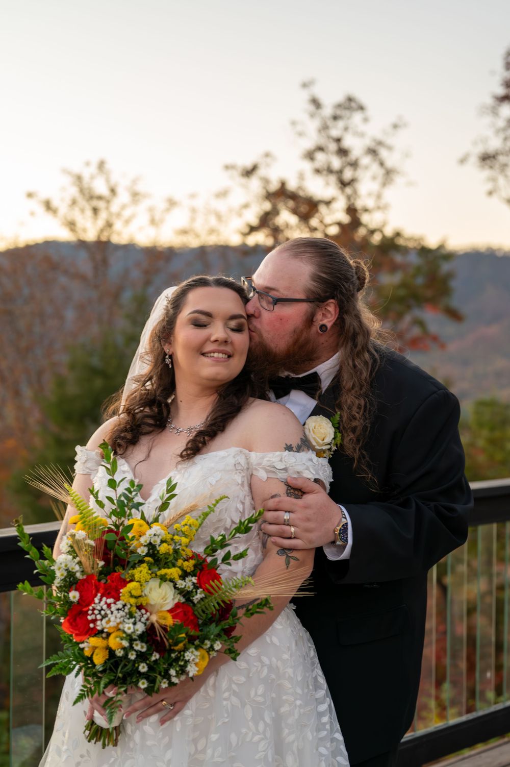 A romantic wedding portrait on a scenic mountain overlook at sunset with a vibrant fall bouquet.