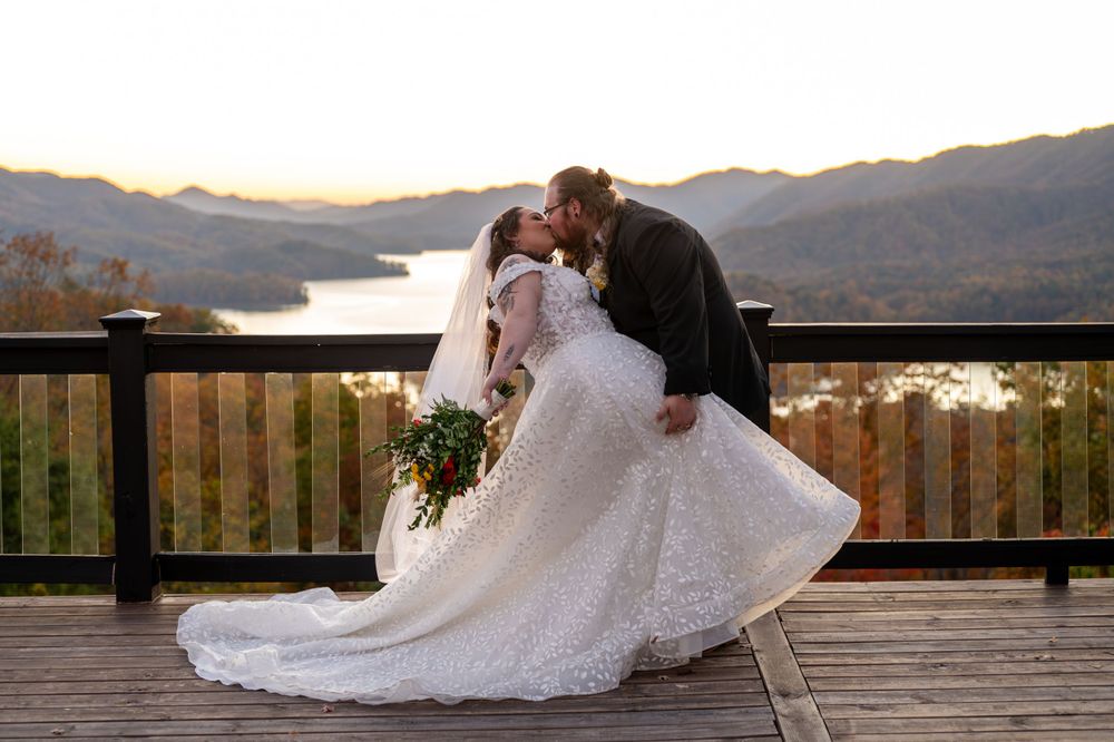 A romantic wedding dip pose on a scenic mountain deck overlooking a lake at sunset.