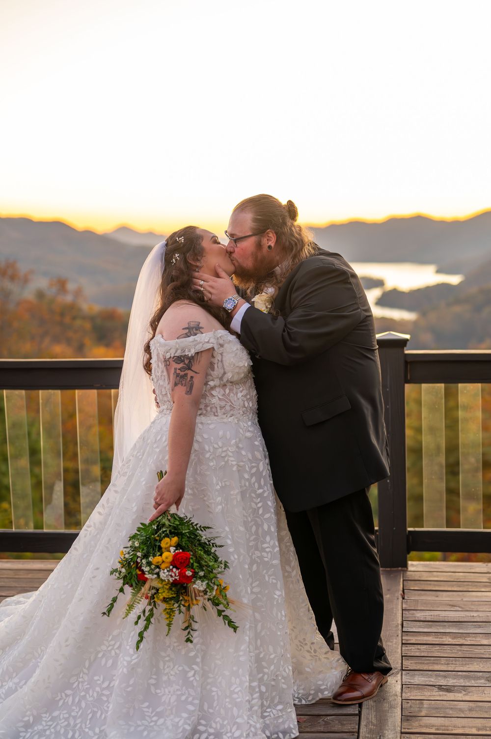A tender wedding moment captured on a wooden deck with mountain and lake views at dusk.