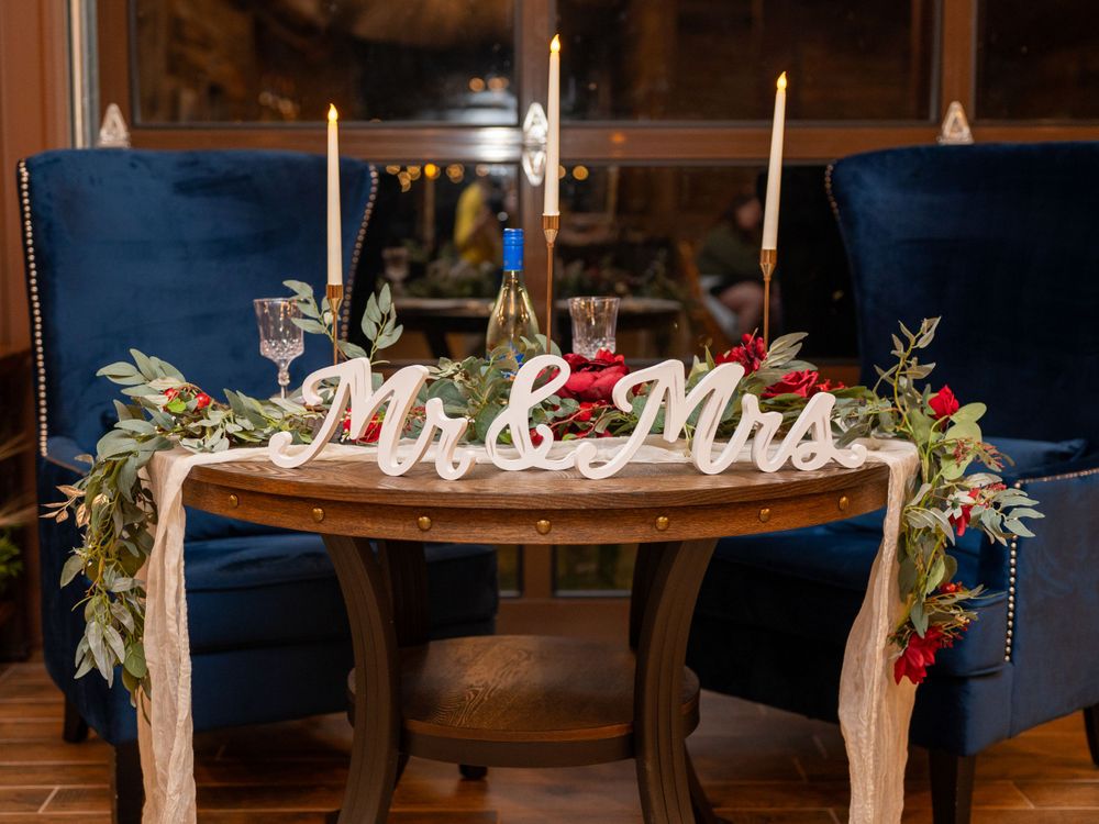 Elegant wedding sweetheart table with Mr & Mrs sign and navy chairs decorated with greenery.