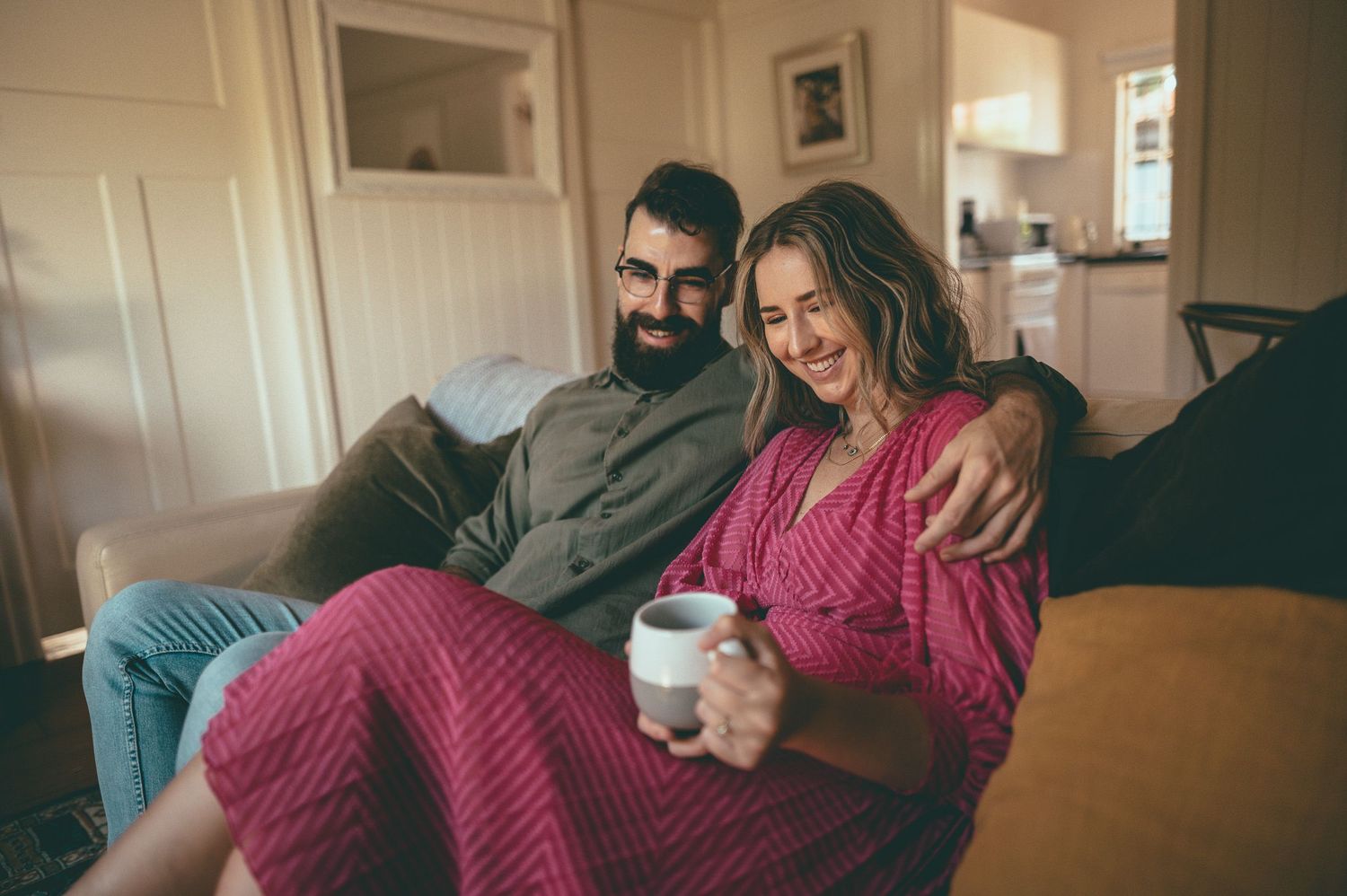 Cozy couple relaxing on sofa at home wearing knit sweaters and sharing a warm drink.