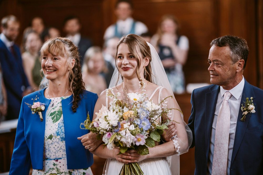 Wedding ceremony in ornate wood-paneled hall with chandelier and guests.