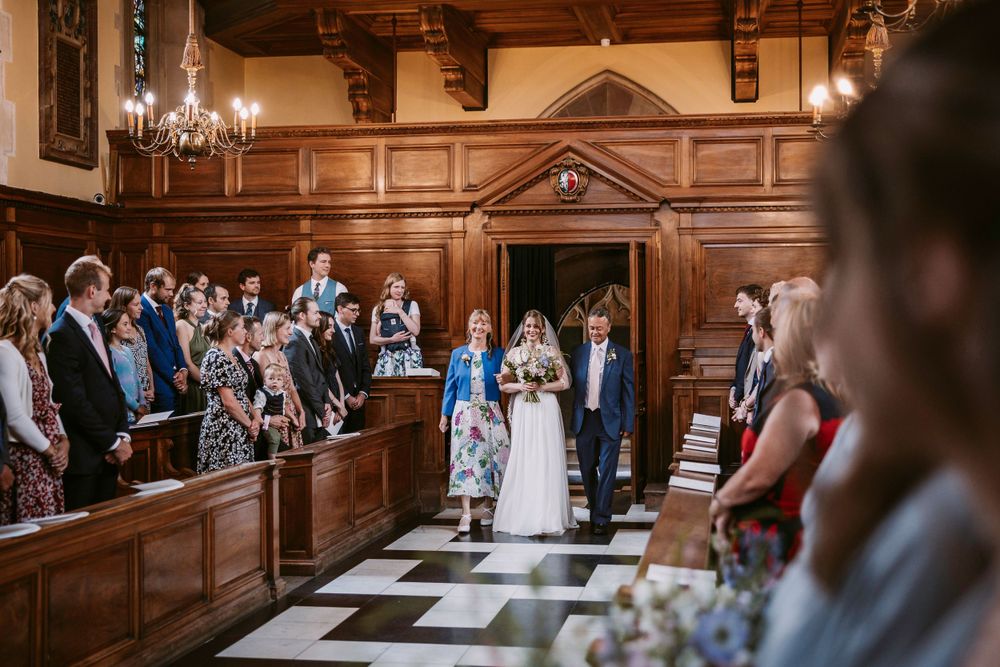 Bride enters Wedding ceremony in historic chapel with checkerboard floor and wooden pews at Balliol College, Oxford.