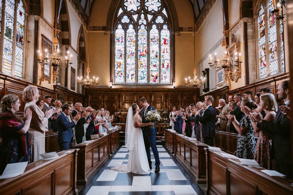 Wedding ceremony in grand chapel with stained glass windows and guests filling the pews at Balliol College, Oxford
