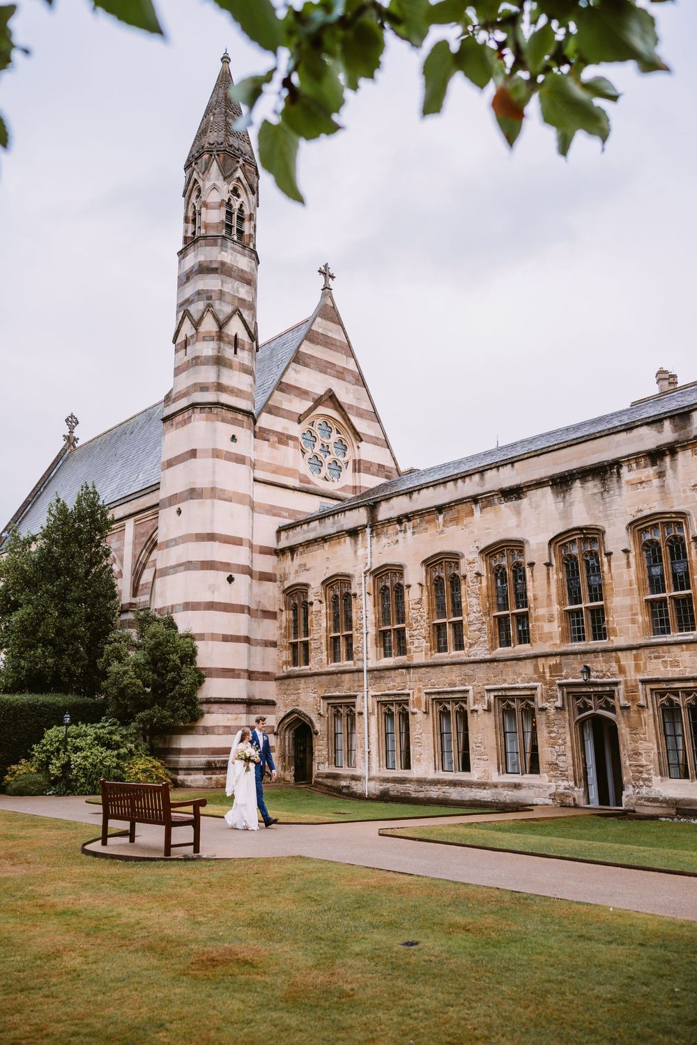 Gothic revival chapel exterior with spire and couple posing on manicured lawn at Balliol College, Oxford