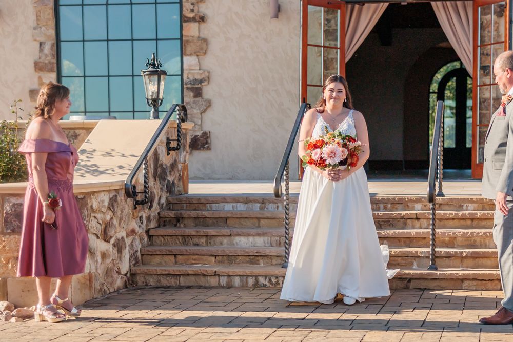 A wedding scene on stone steps of a Spanish-style venue with arched windows.