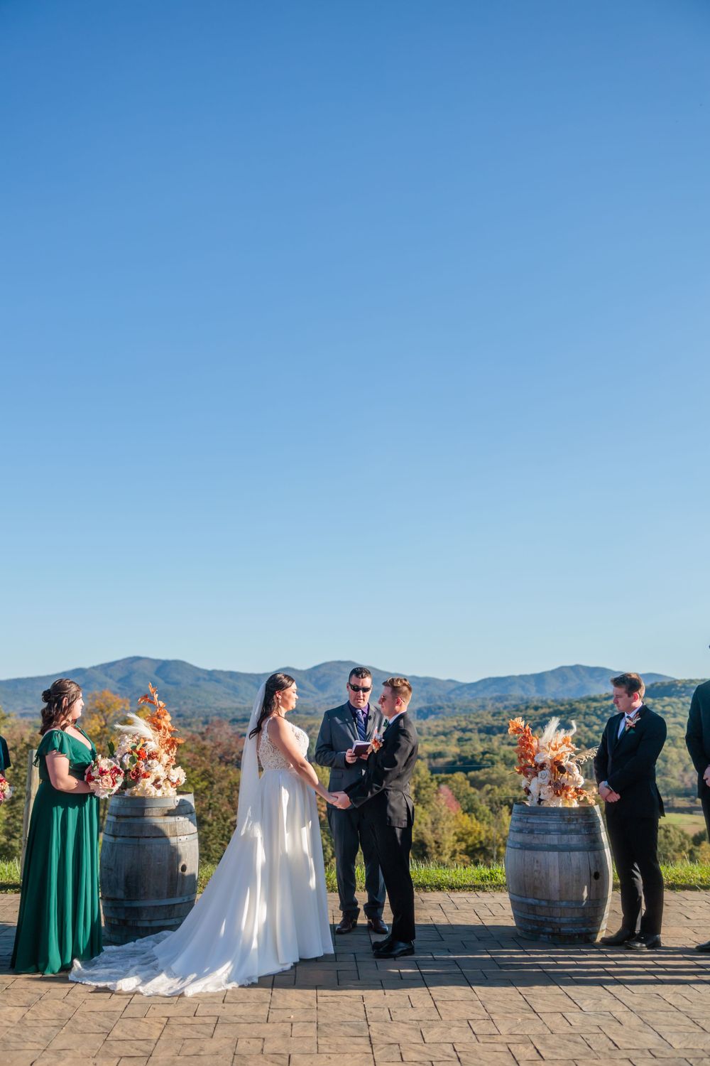 An outdoor wedding ceremony with wine barrels and mountain views in the background.