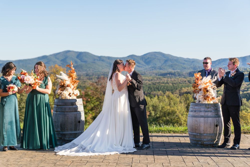 Outdoor wedding ceremony with mountain views and autumn floral arrangements on wine barrels.