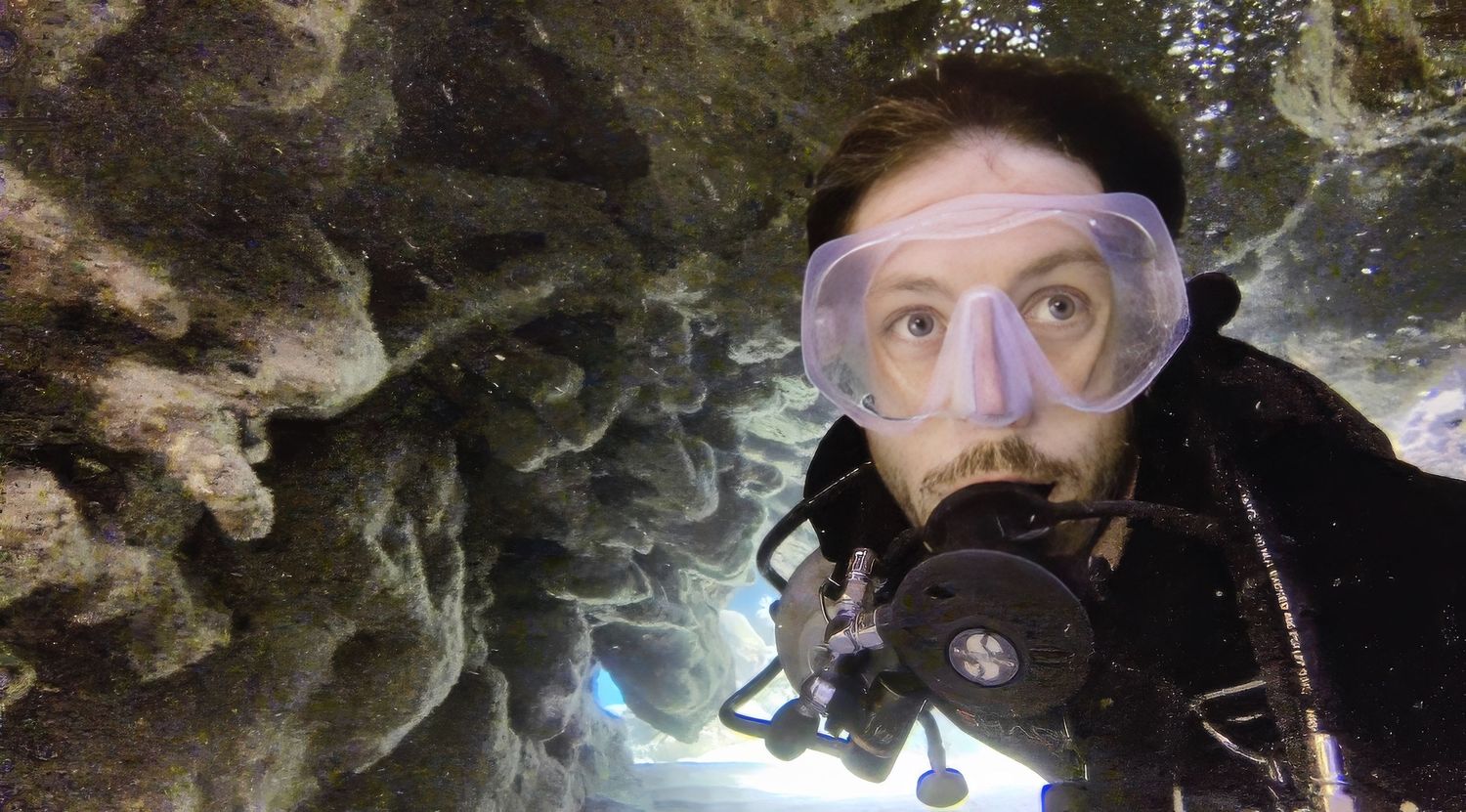 Scuba diver explores underwater cave with rocky formations visible in background side mount diving in confined space. Evan Will diving