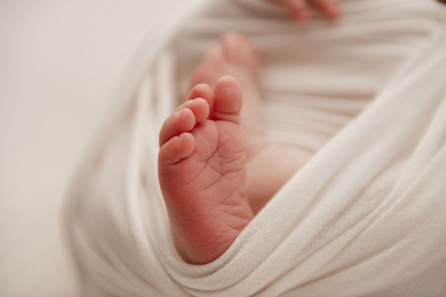 Tiny newborn baby foot wrapped in soft white cloth showing delicate toes and skin texture.