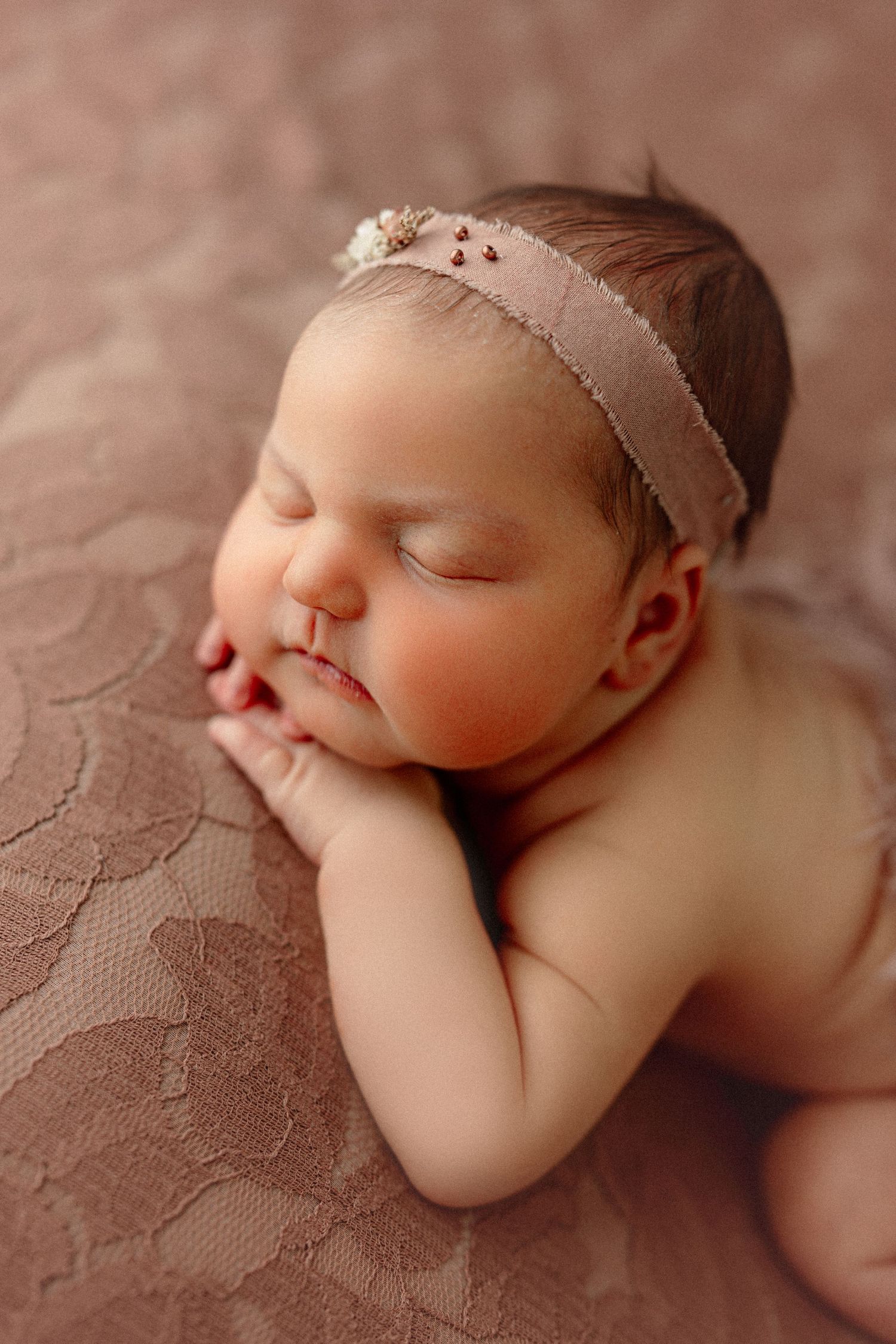 A sleeping newborn baby wearing a delicate headband rests on textured beige bedding in artistic close-up photos.