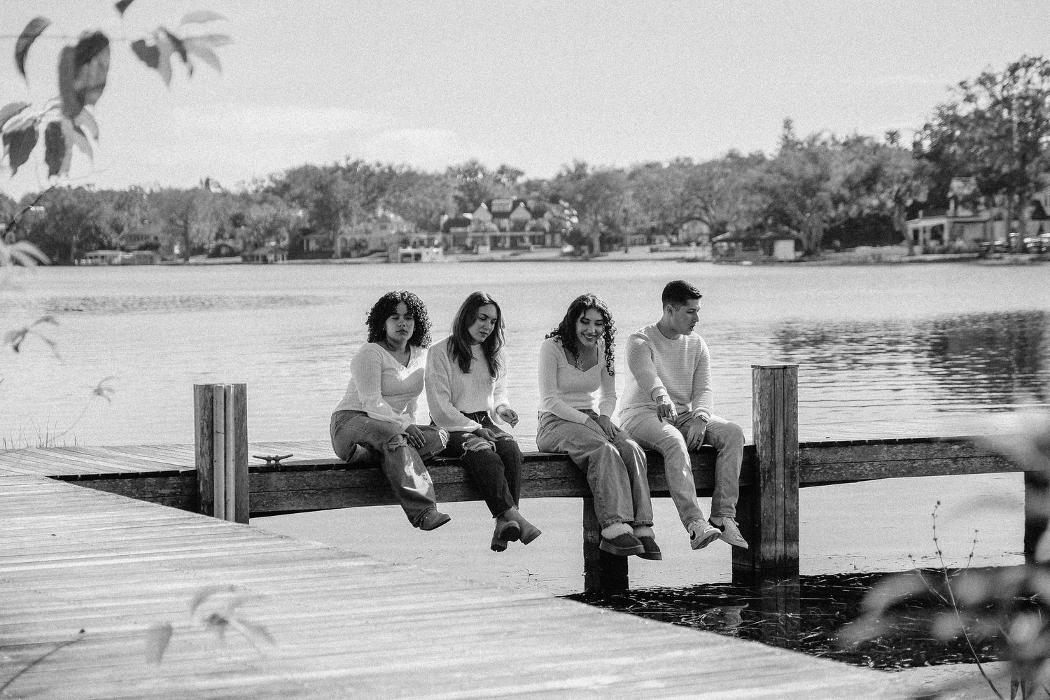 People sitting on wooden dock overlooking water in black and white.