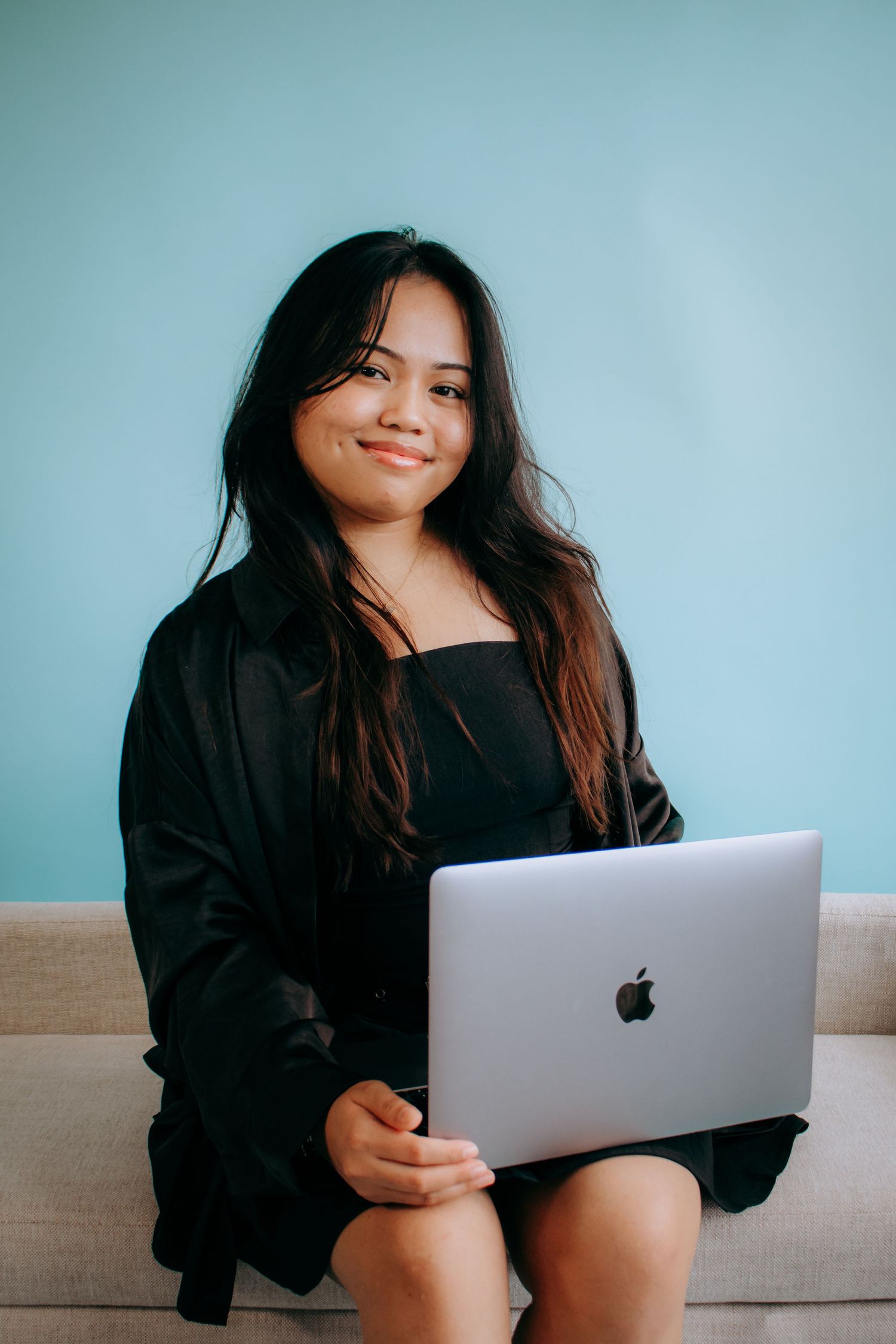 Person in black clothing relaxing on couch while working on MacBook laptop.