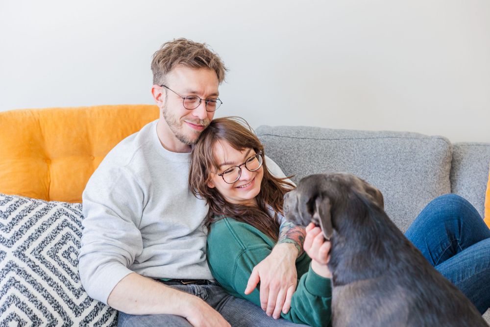 Couple cuddling on orange and grey sectional with their dogs.