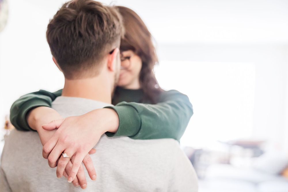 Couple shares tender embrace on light colored sofa.