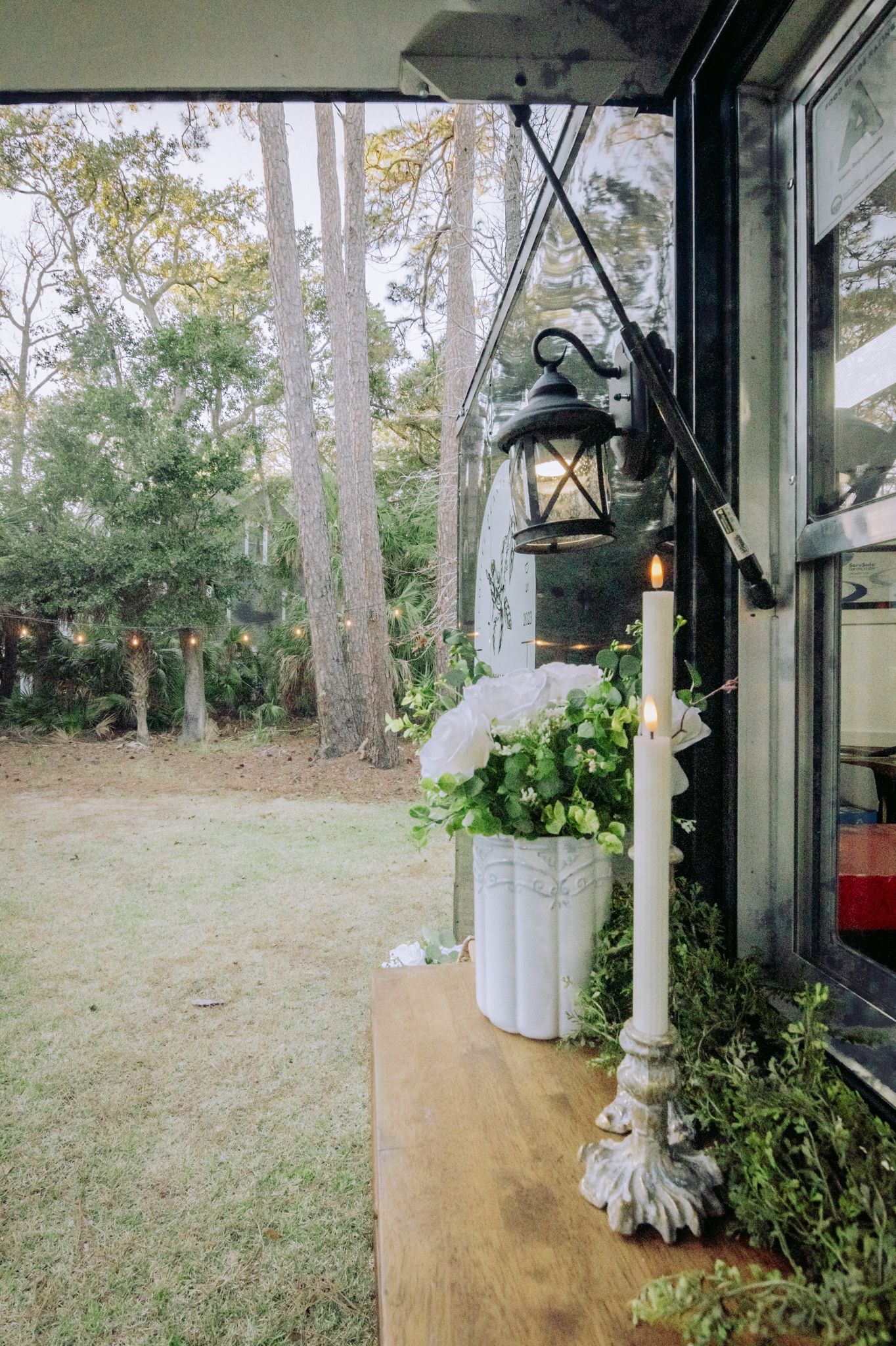 Vintage lantern and potted plants on wooden ledge with forest backdrop.